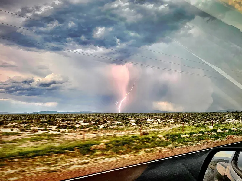Pink lightning beneath dark storm clouds over flat land