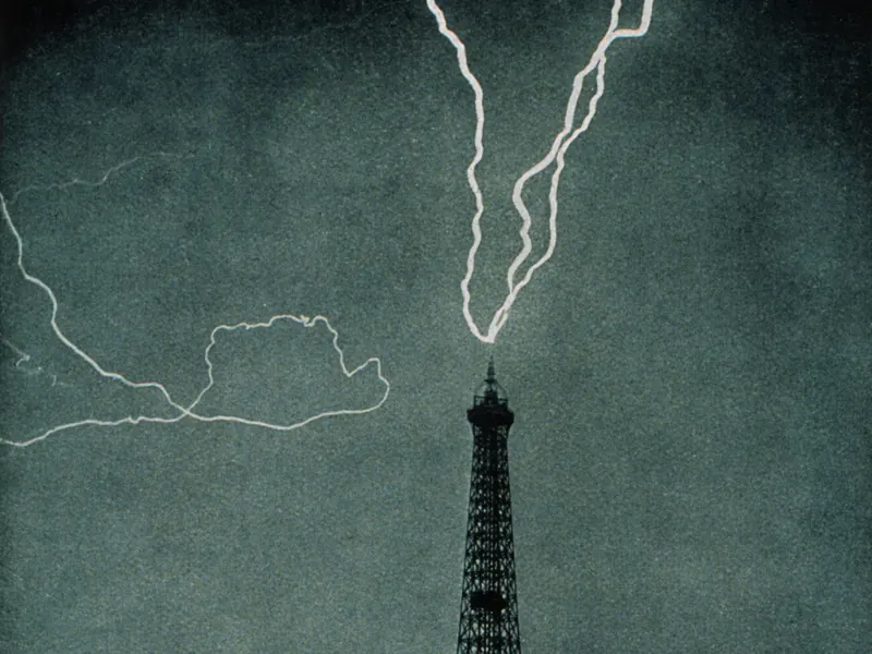 An old black-and-white photo of lightning striking the top of the Eiffel Tower at night