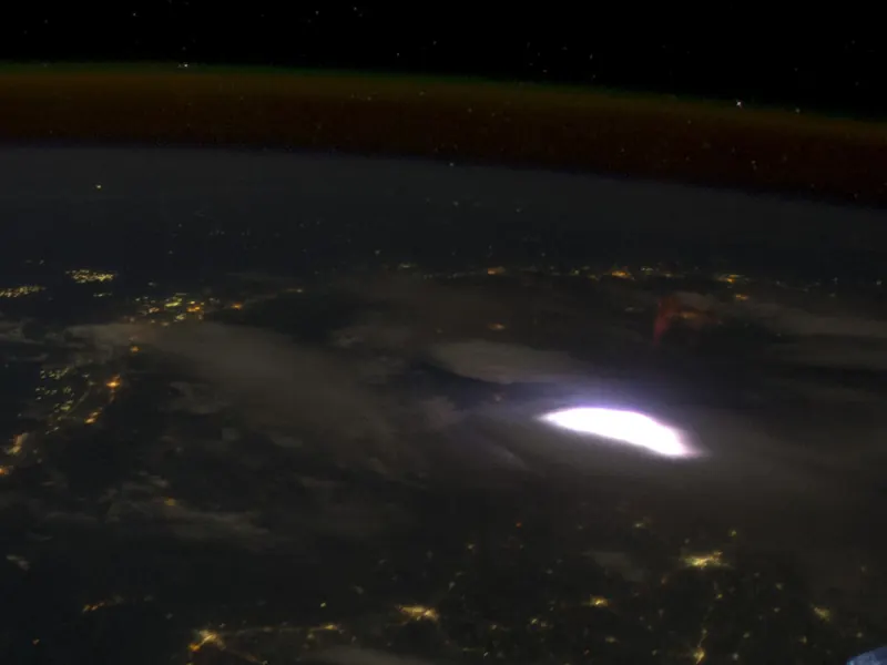 A view from orbit of Earth at night with a faint glow above the clouds