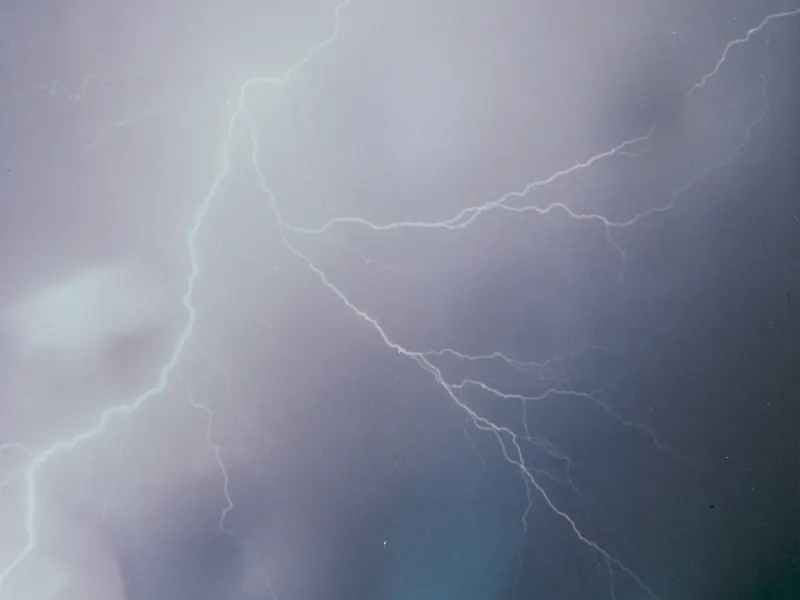 Lightning bolts in a rainy sky above a lit launch pad