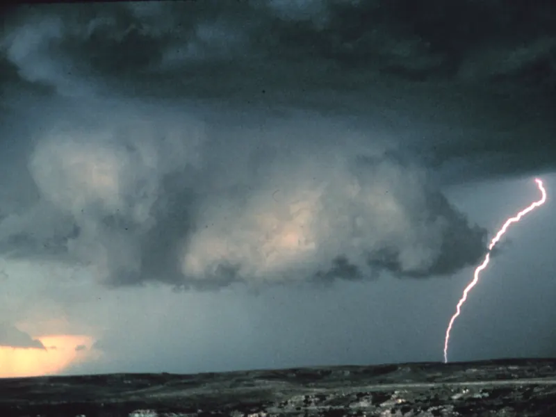 A low, dark wall cloud with a lightning bolt beneath it